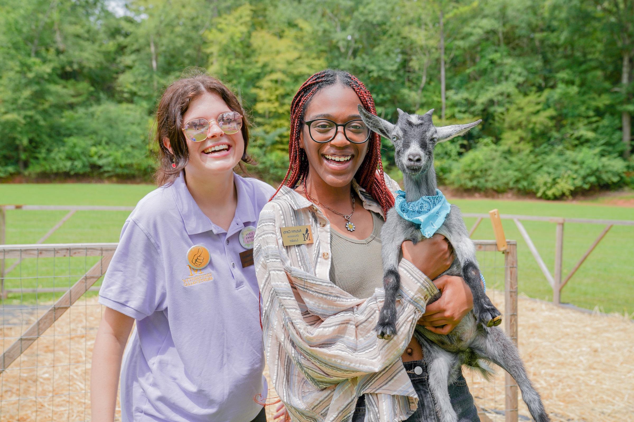 Photo of two female students holding a goat at goat yoga event.